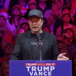 Elon Musk is on the stage wearing his Dark Gothic MAGA hat.2